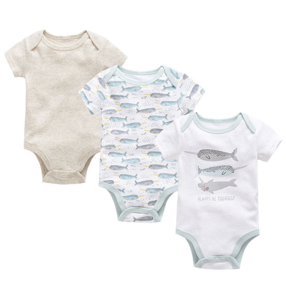 Three soft cotton baby bodysuits: one beige, one white with narwhal print, and one white with "Always Be Yourself" shark design.