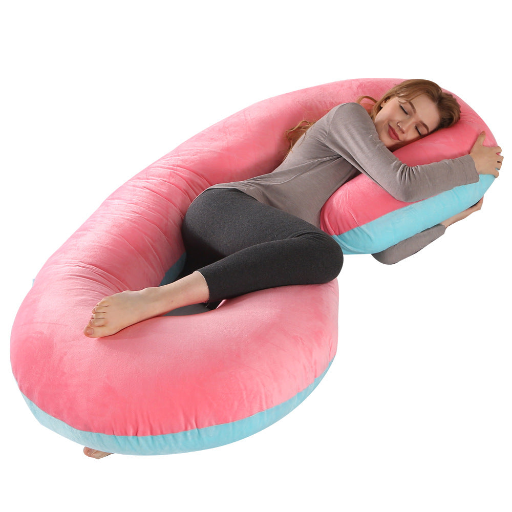 Velvet C-shaped pregnancy pillow in pink and blue, supporting a woman sleeping comfortably.