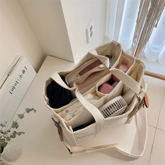 Stylish beige canvas diaper bag with multiple compartments, a fan, and baby essentials.