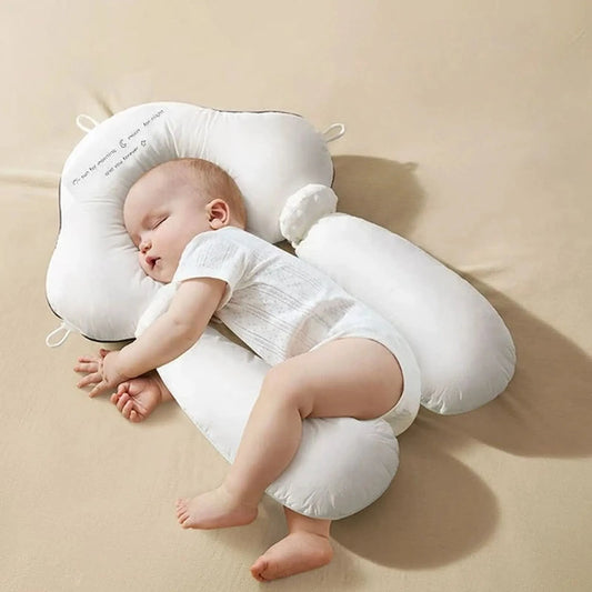White ergonomic baby sleep pillow with side bolsters supporting a sleeping infant.