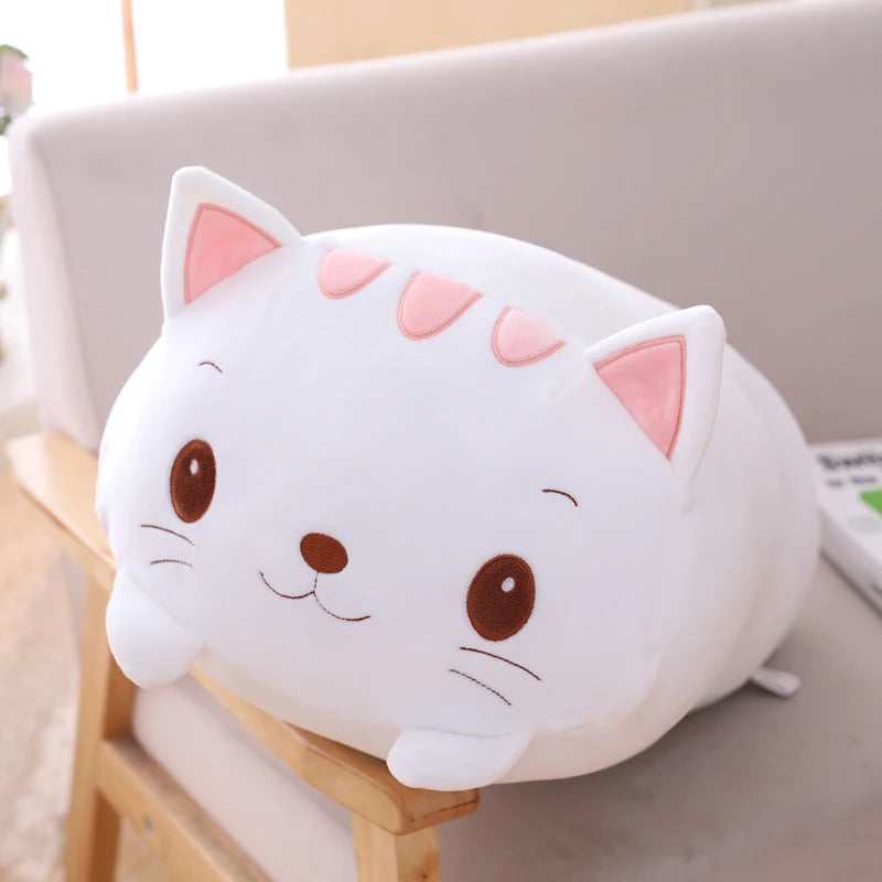 Soft white plush cat pillow with pink ears and brown embroidered eyes, resting on a sofa.