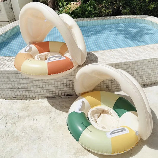 Two inflatable baby swim floats with sun canopies, one in orange/cream/yellow, the other in green/yellow/cream, by a pool.