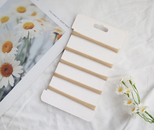 Set of six beige elastic cotton headbands for babies and toddlers, displayed on a white card.