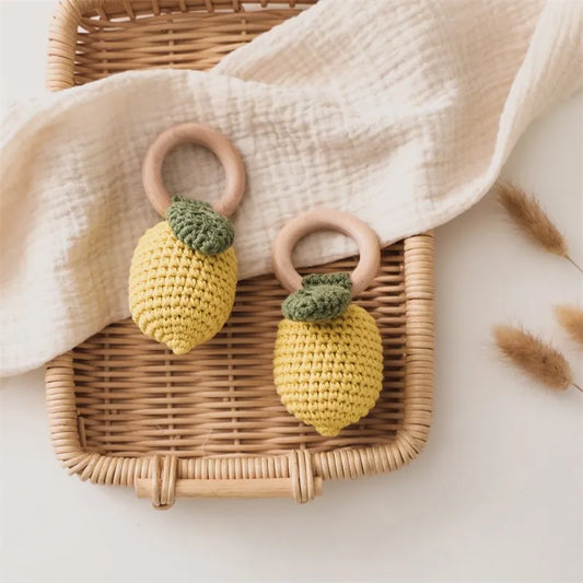 Two yellow crocheted lemon rattles with green leaves and natural wooden rings on a woven tray.