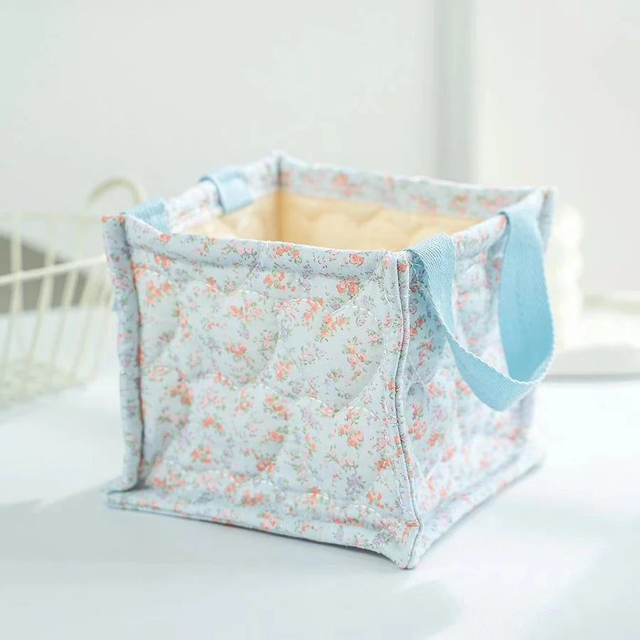 Square quilted light blue storage basket with delicate floral print and blue fabric handles.