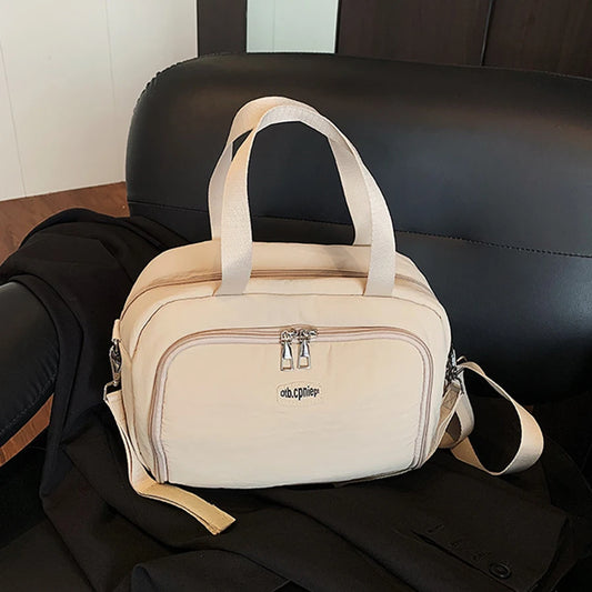 Beige polyester diaper bag with top handles, front zip pocket, and shoulder strap, resting on a black chair.