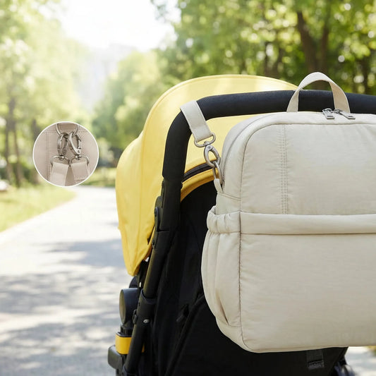 Beige multi-functional diaper bag attached to a yellow stroller, featuring side pockets and a secure zipper closure.