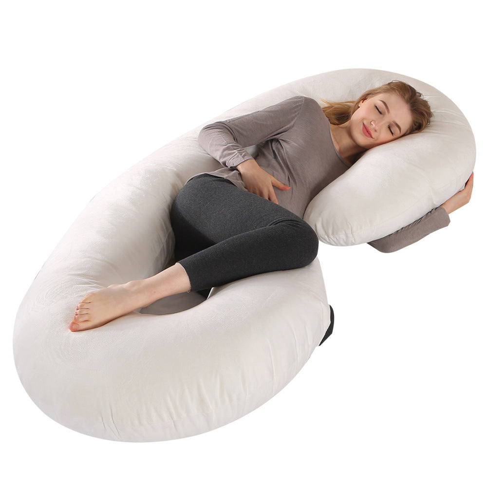 Pregnant woman sleeping soundly on a large, white C-shaped velvet pregnancy pillow, supporting her body.