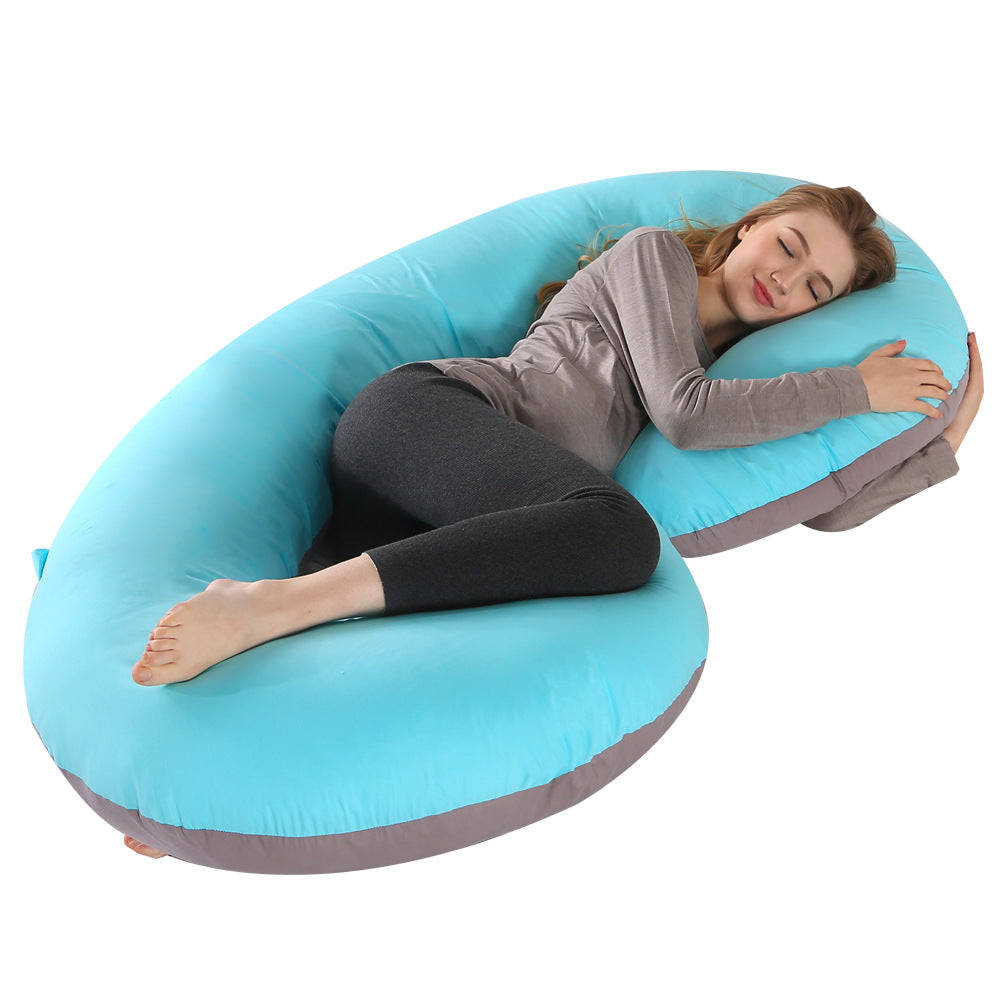 Pregnant woman sleeping peacefully on a large, C-shaped blue and grey velvet full body pillow.