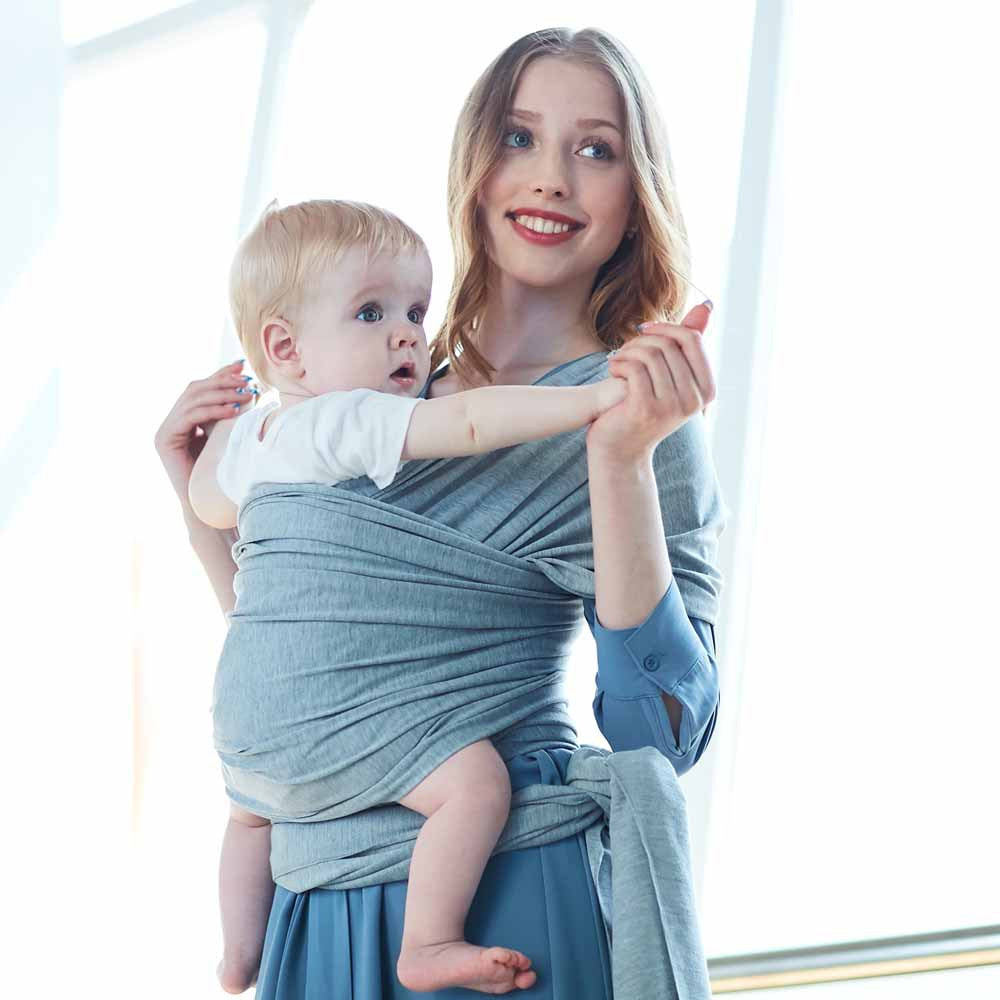 Smiling woman carrying a baby in a soft, breathable gray cotton baby wrap.