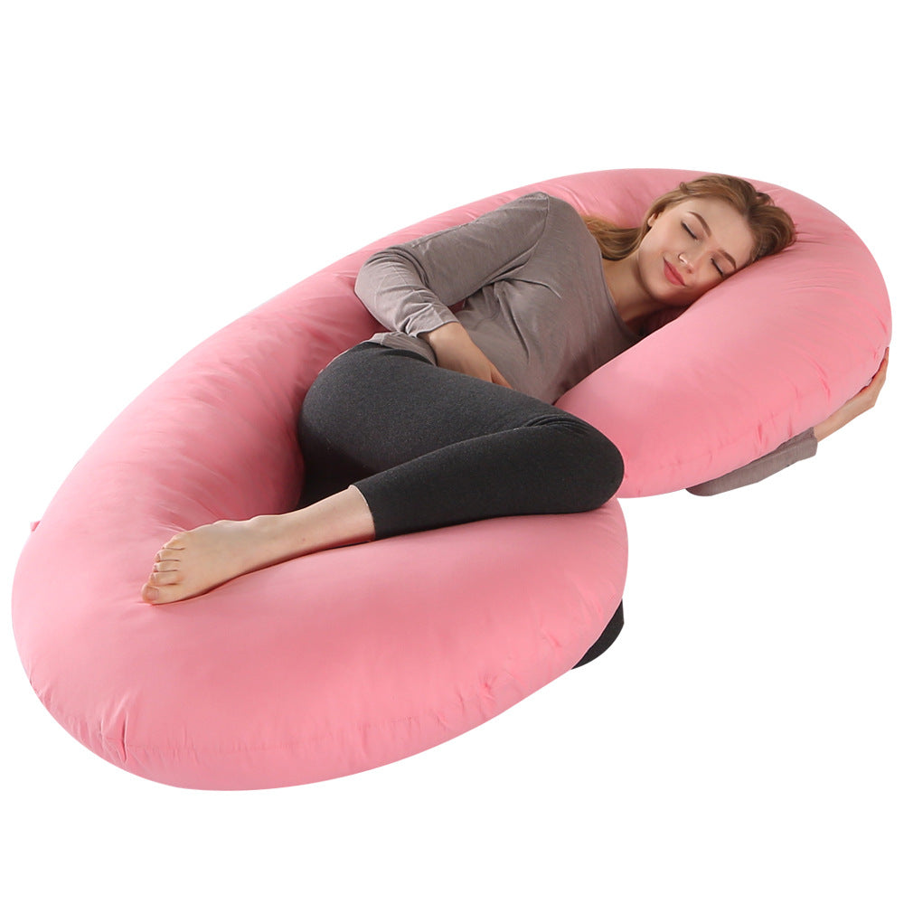 Pregnant woman sleeping comfortably on a large pink C-shaped velvet full body maternity pillow.