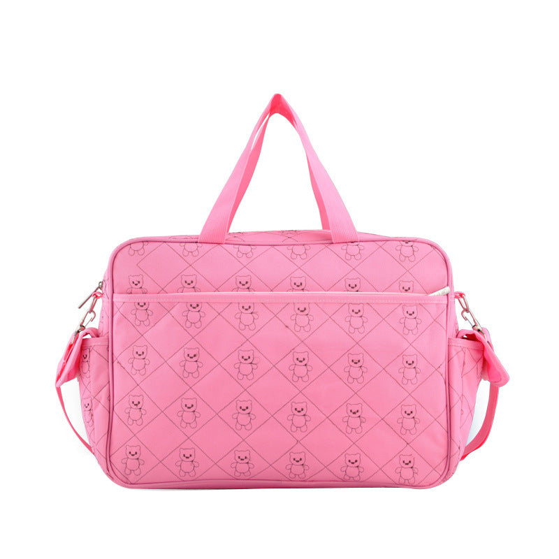 Pink polyester diaper bag with quilted teddy bear pattern, top handles, and shoulder strap.
