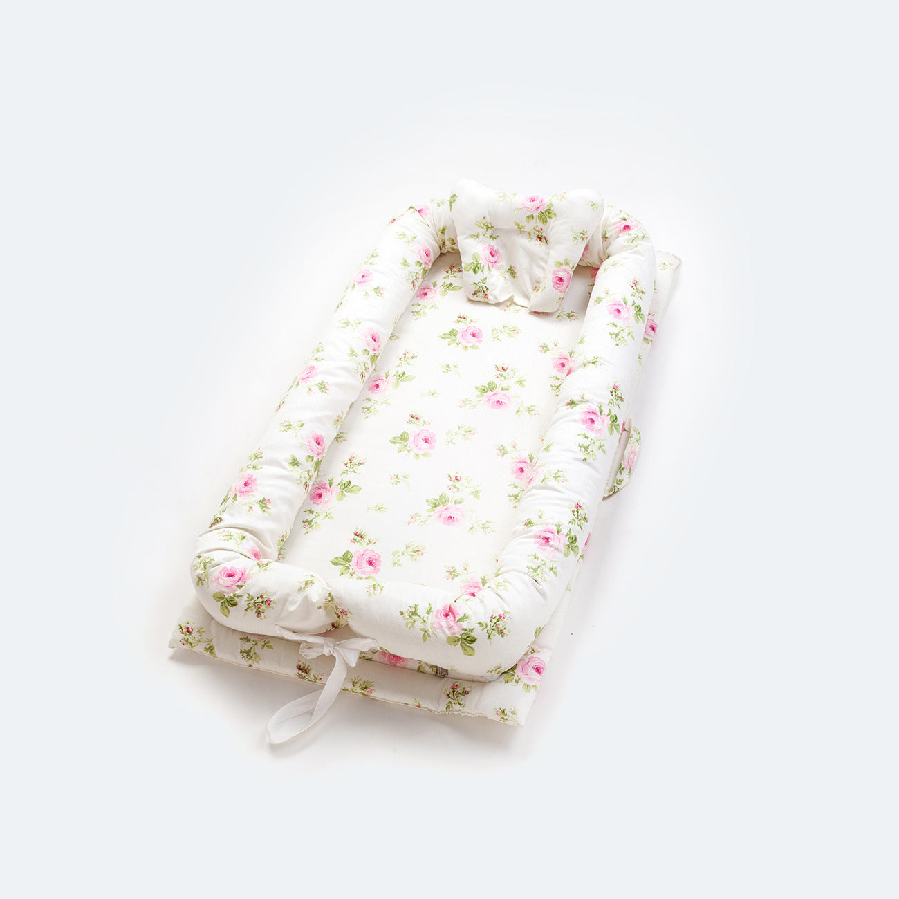 Portable cotton baby nest with pink floral pattern, head support, and padded sides.