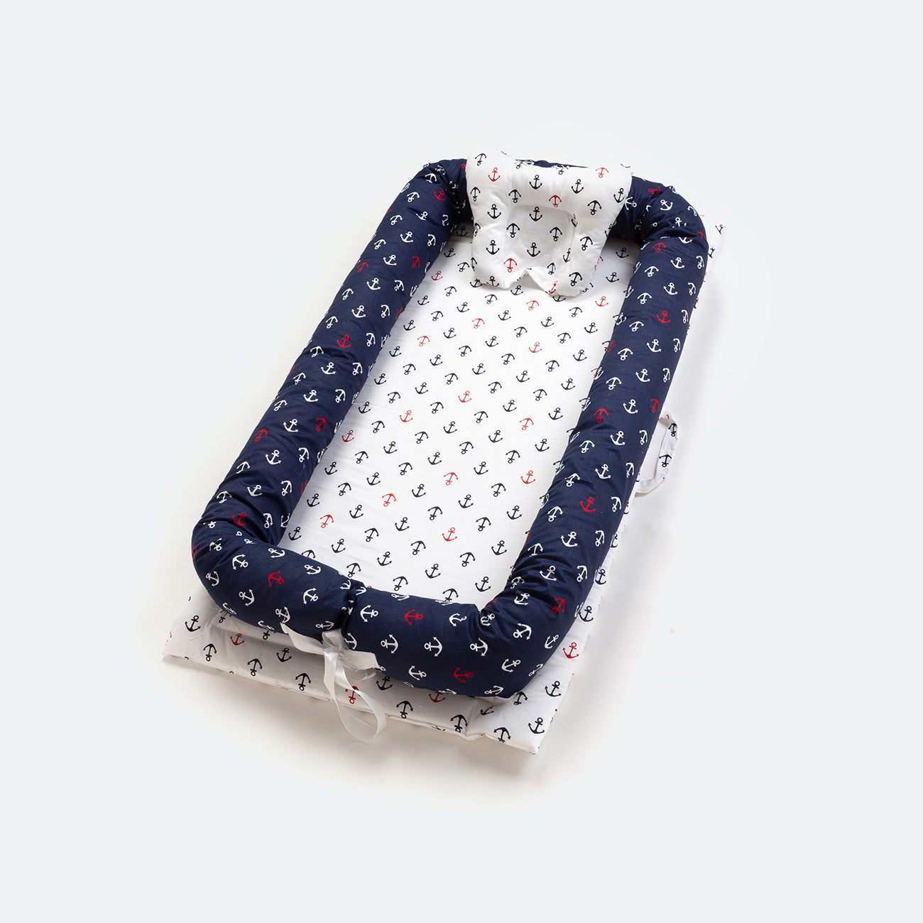 Navy and white cotton portable baby nest with red and navy anchor print, head protector, and padded sides.