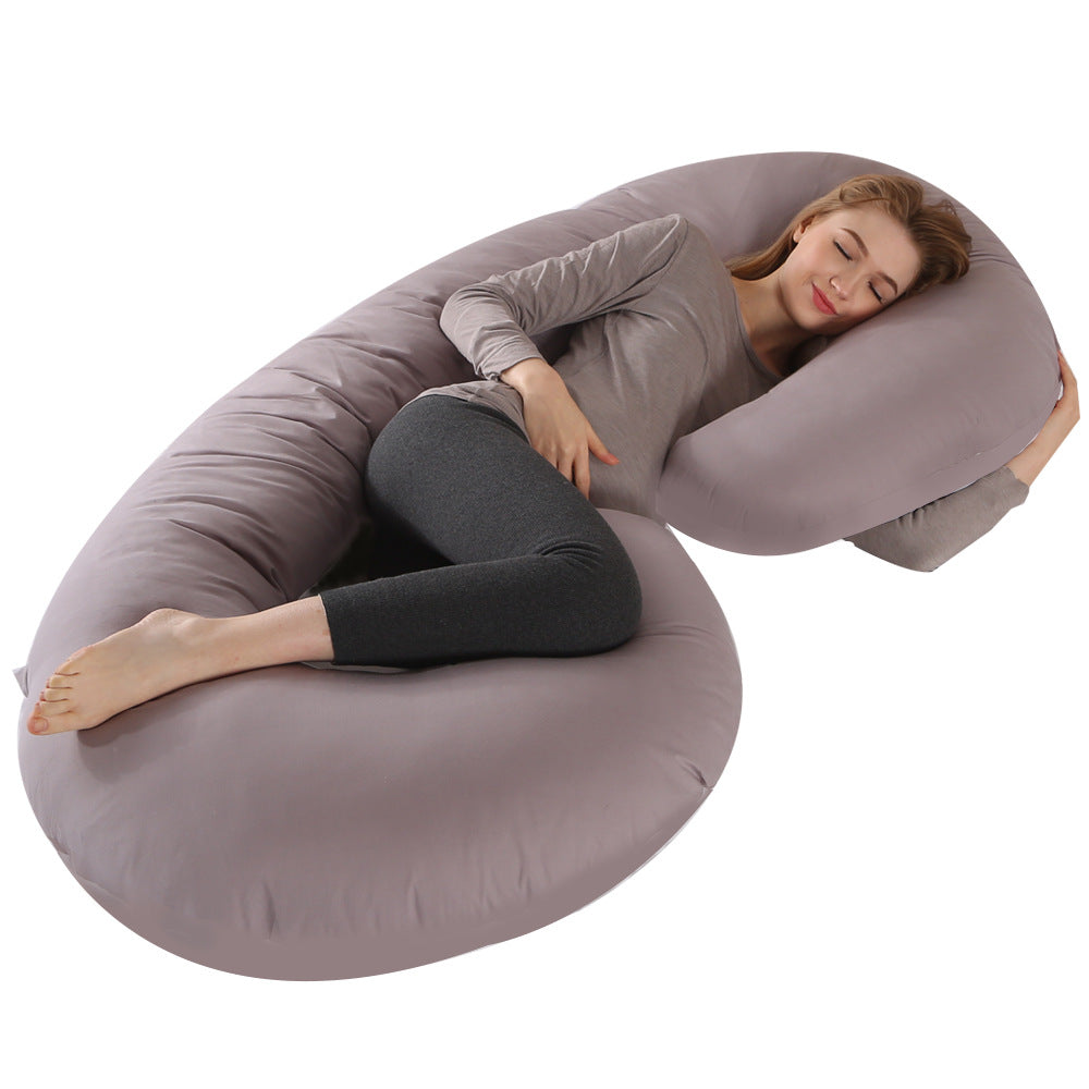 Pregnant woman sleeping comfortably on a large, grey C-shaped velvet maternity pillow.