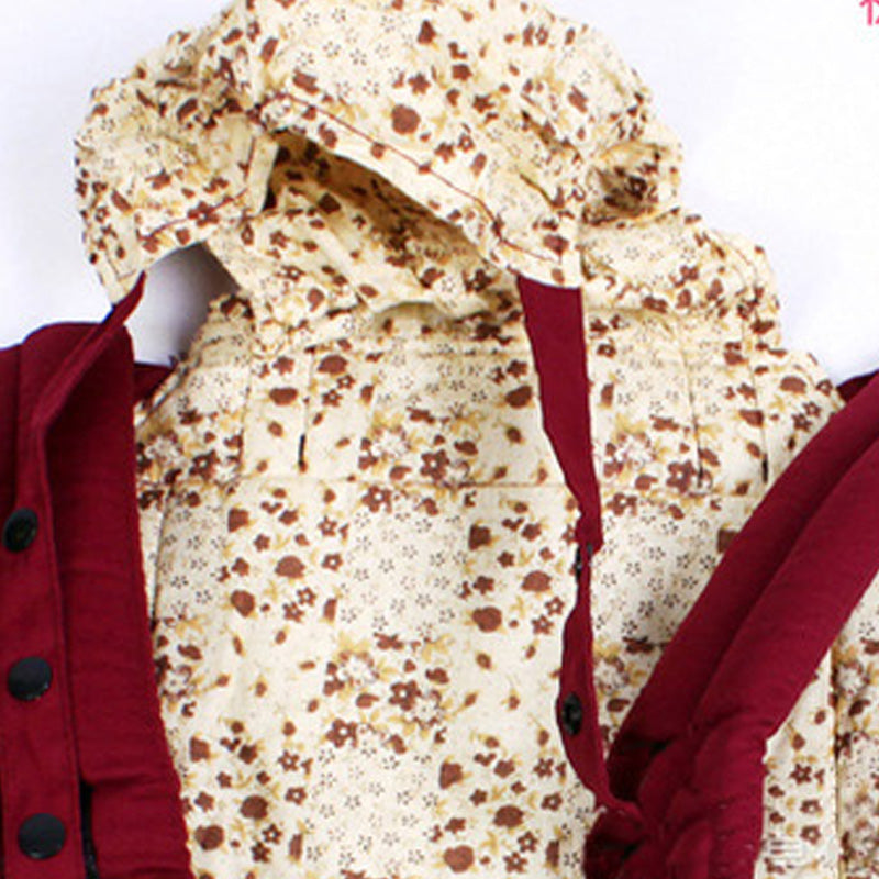 Ergonomic cotton baby carrier in red with a cream floral pattern, featuring a hood and padded straps.