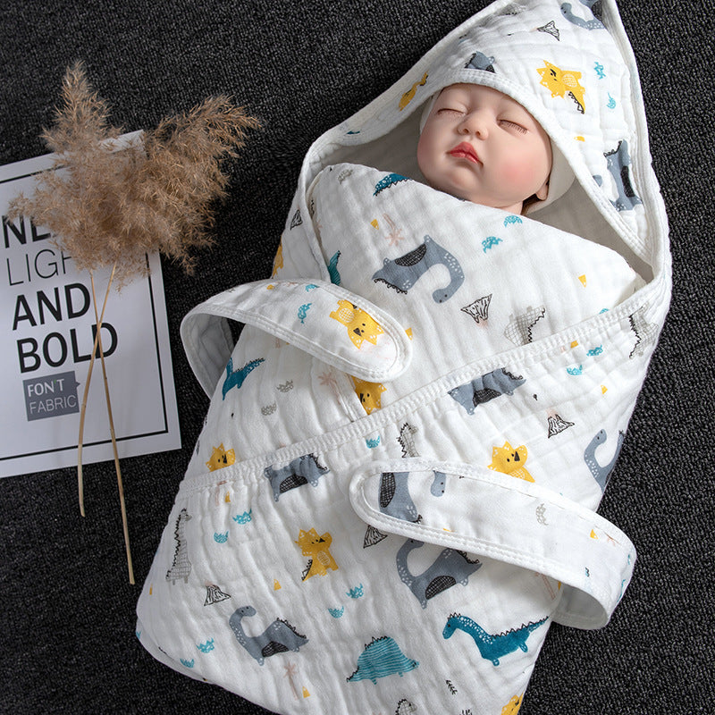 White cotton gauze baby swaddle with hood, featuring colorful dinosaur patterns, wrapped around a doll.