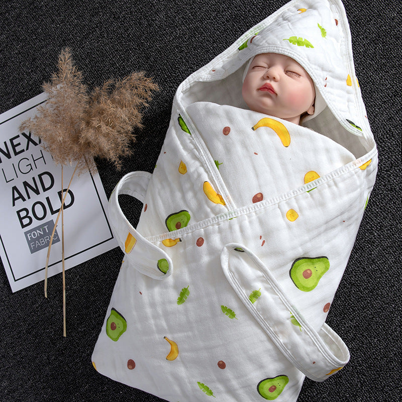 White cotton gauze baby swaddle with avocado and banana print, featuring a hooded design and carrying straps.