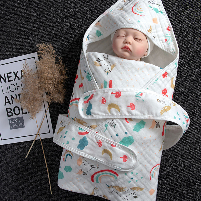 White cotton gauze baby swaddle with hood, colorful unicorn and rainbow print, and adjustable velcro.