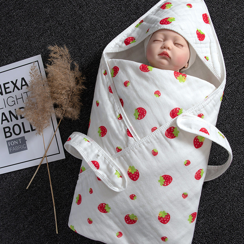 White cotton gauze baby swaddle with red strawberry print, featuring a hooded design and a sleeping doll.
