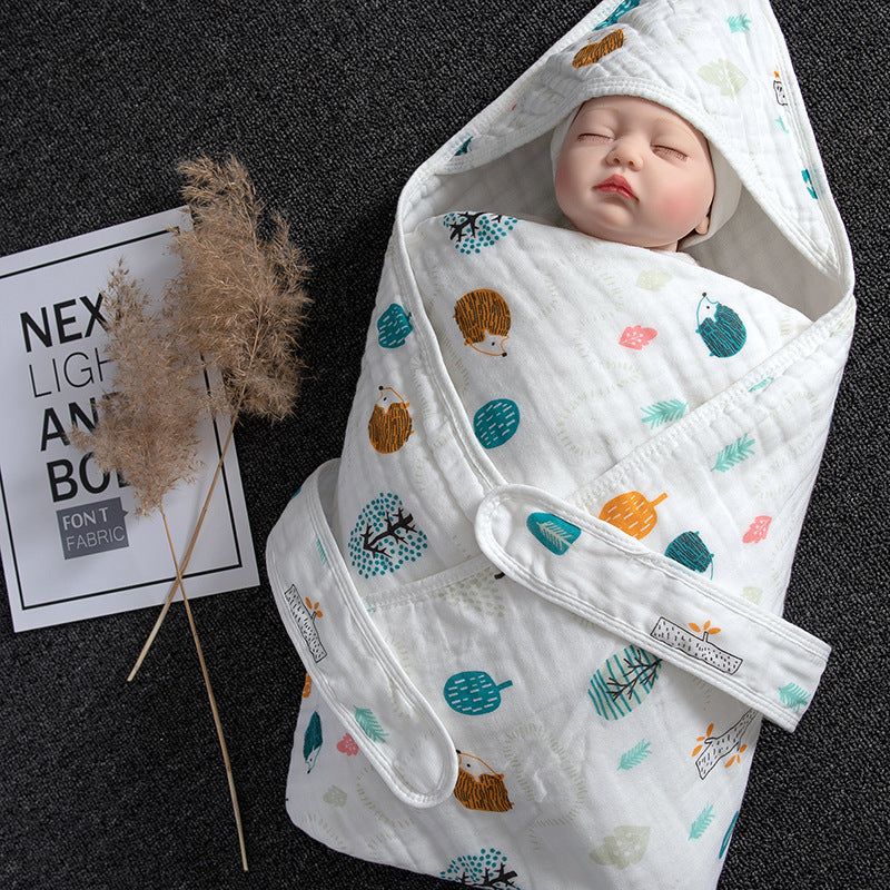 White cotton gauze baby swaddle with hedgehog and leaf print, featuring a hood and secure straps.