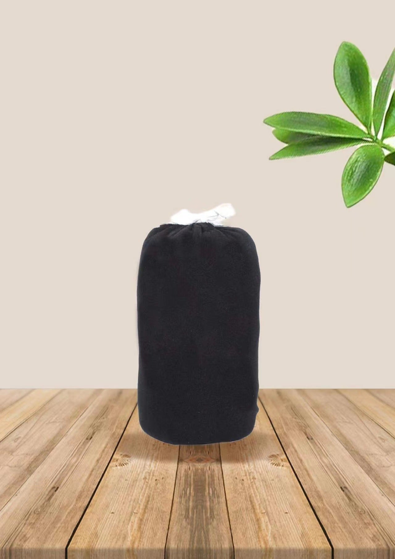 Folded black soft ergonomic baby wrap carrier on a wooden surface with green leaves.
