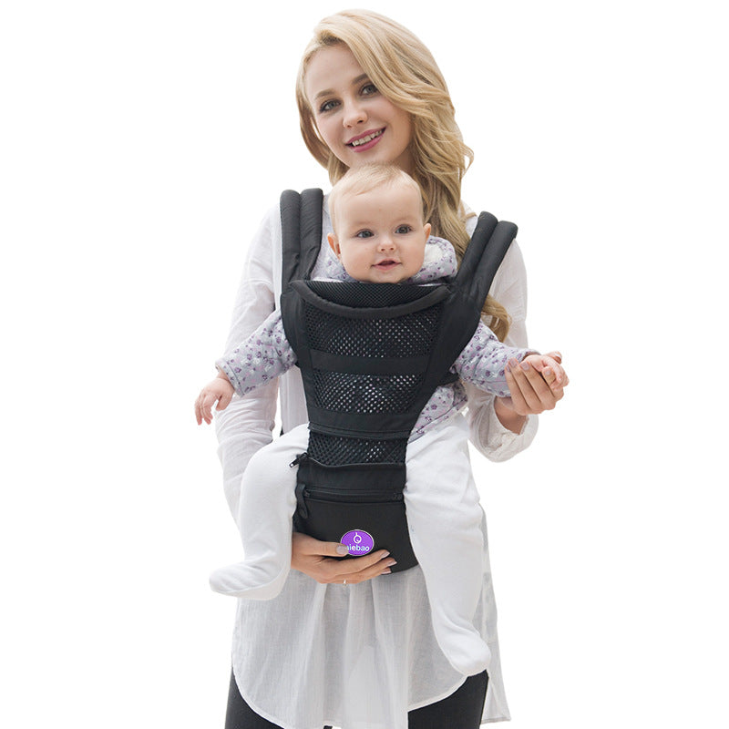 Smiling mother holding baby in a black ergonomic multi-functional baby carrier with a hip seat.