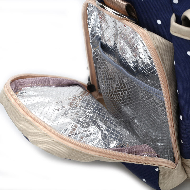 Navy polka dot diaper backpack with beige trim, showing an open insulated side pocket.