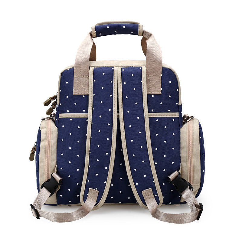 Navy blue polka dot diaper backpack with beige accents, padded straps, and side pockets.