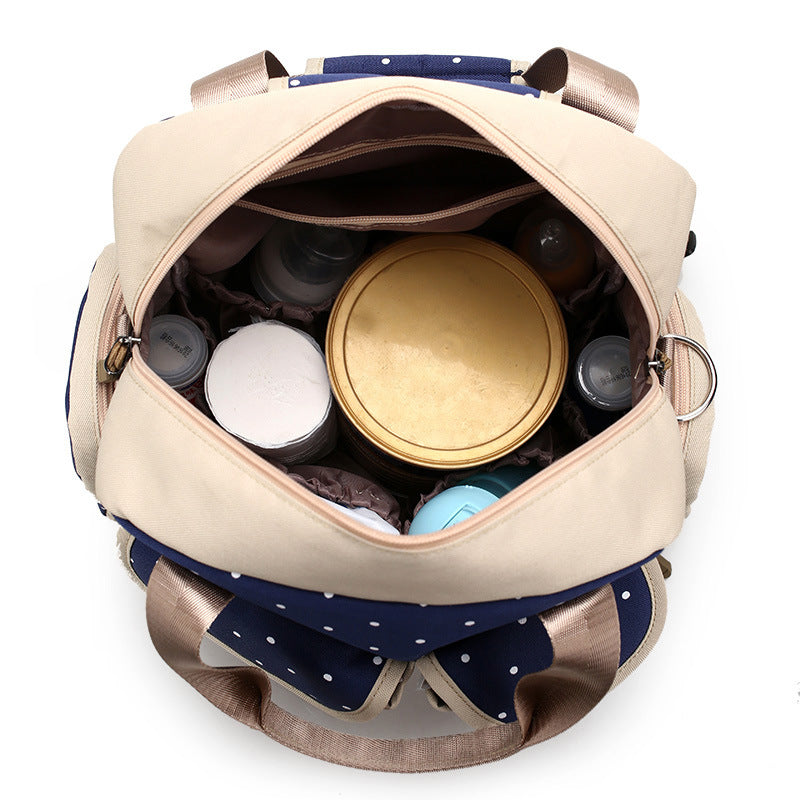 Open beige and navy polka dot diaper backpack with multiple compartments and baby bottles.