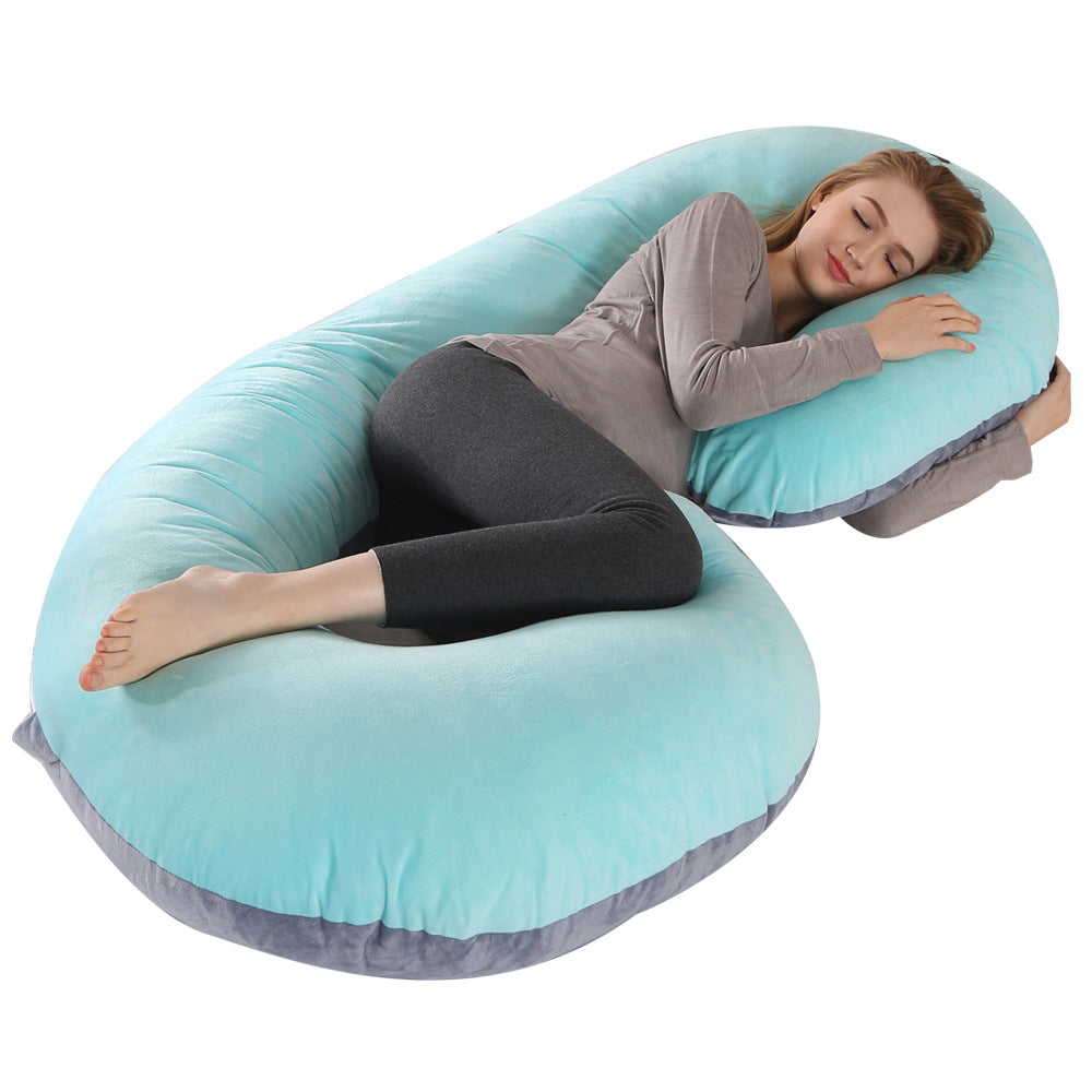 Pregnant woman sleeping soundly on a large, C-shaped teal velvet maternity pillow with gray trim.