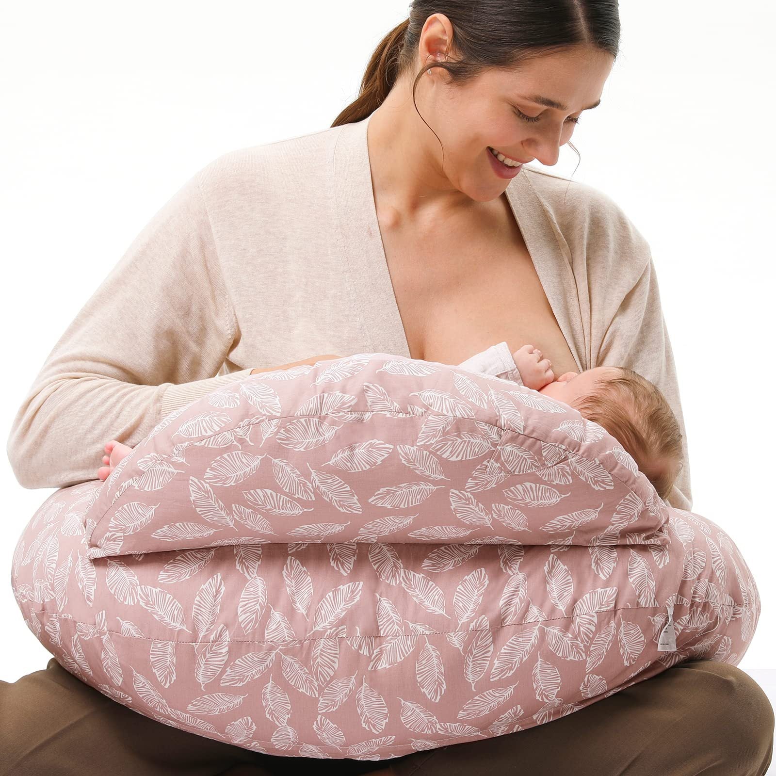 Woman breastfeeding baby using a pink multi-use nursing pillow with white feather print.