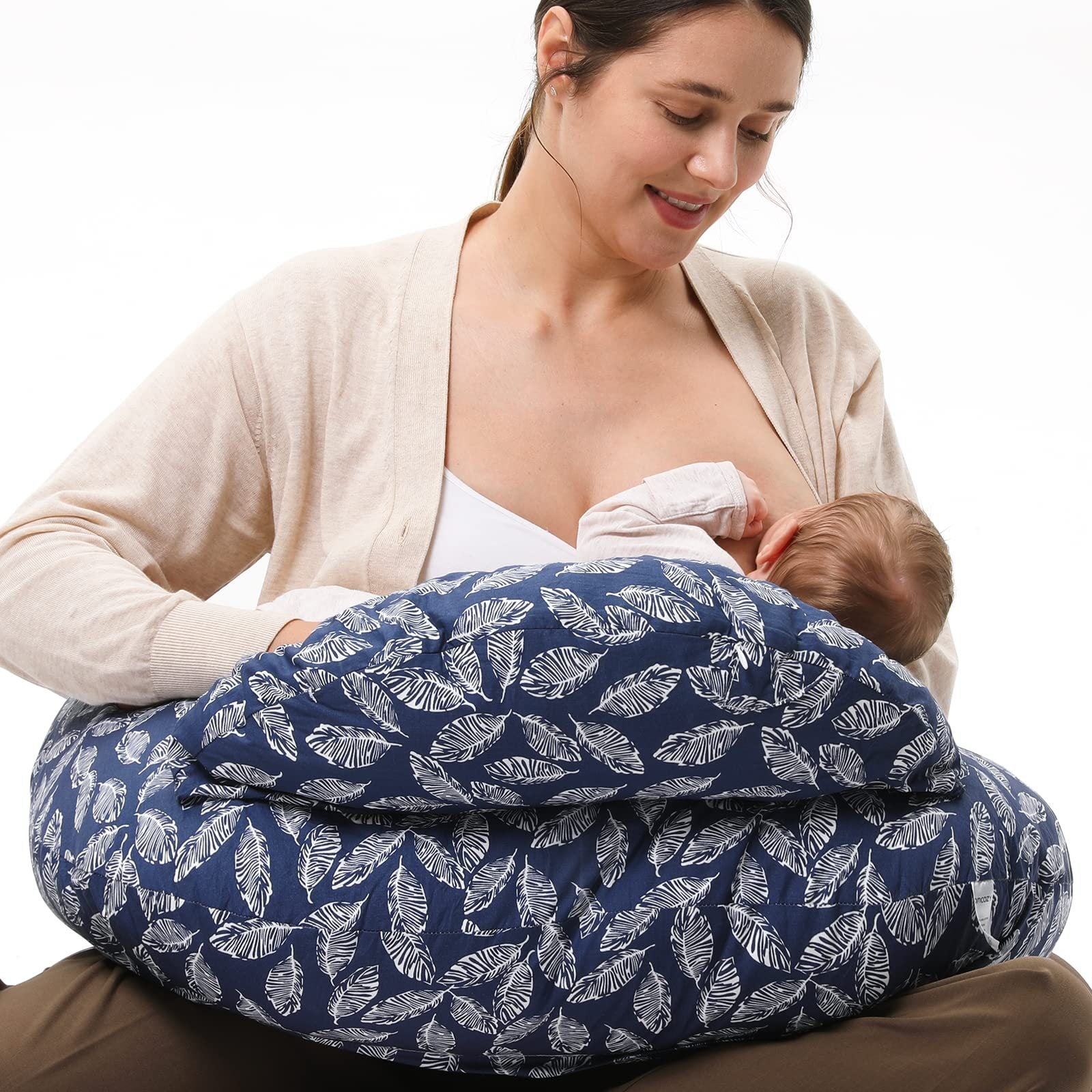 Smiling mother breastfeeding baby using a blue nursing pillow with white leaf print.
