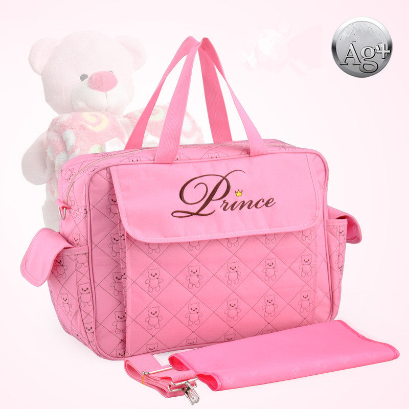 Pink polyester diaper bag with "Prince" embroidery, quilted teddy bear pattern, side pockets, and matching changing pad.