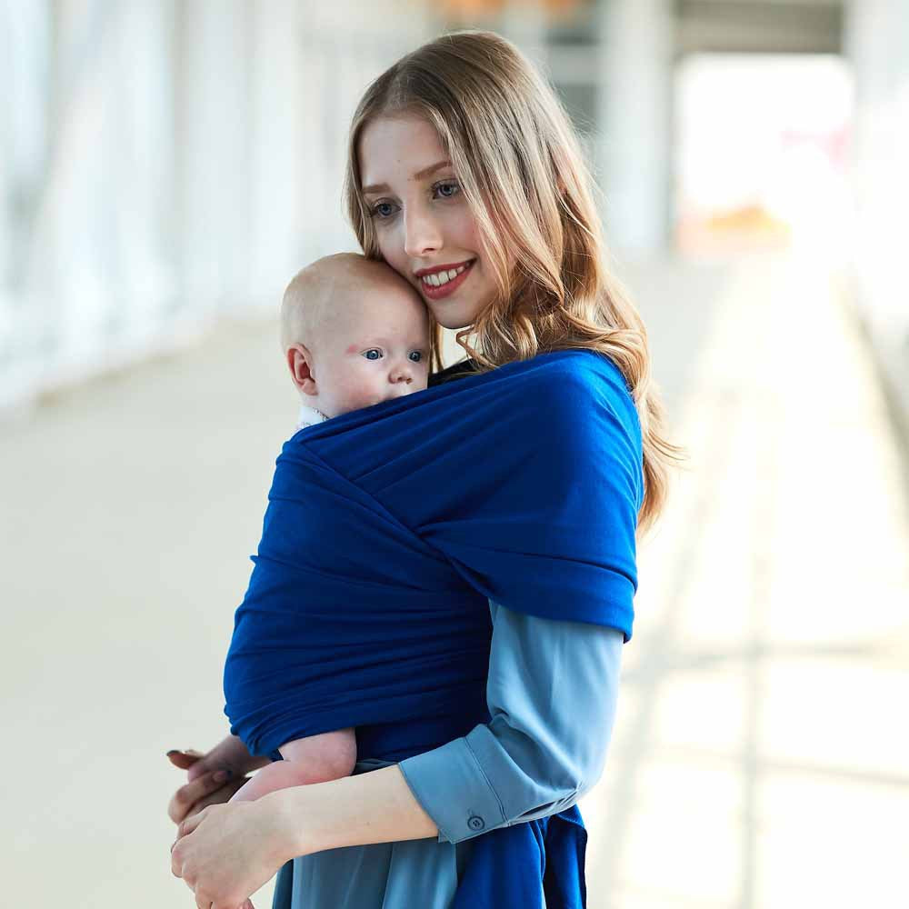 Smiling woman cradling baby in a soft, breathable royal blue cotton baby wrap carrier.