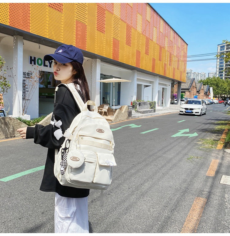 Stylish cream nylon student backpack with laptop compartment, multiple pockets, and checkerboard charm.