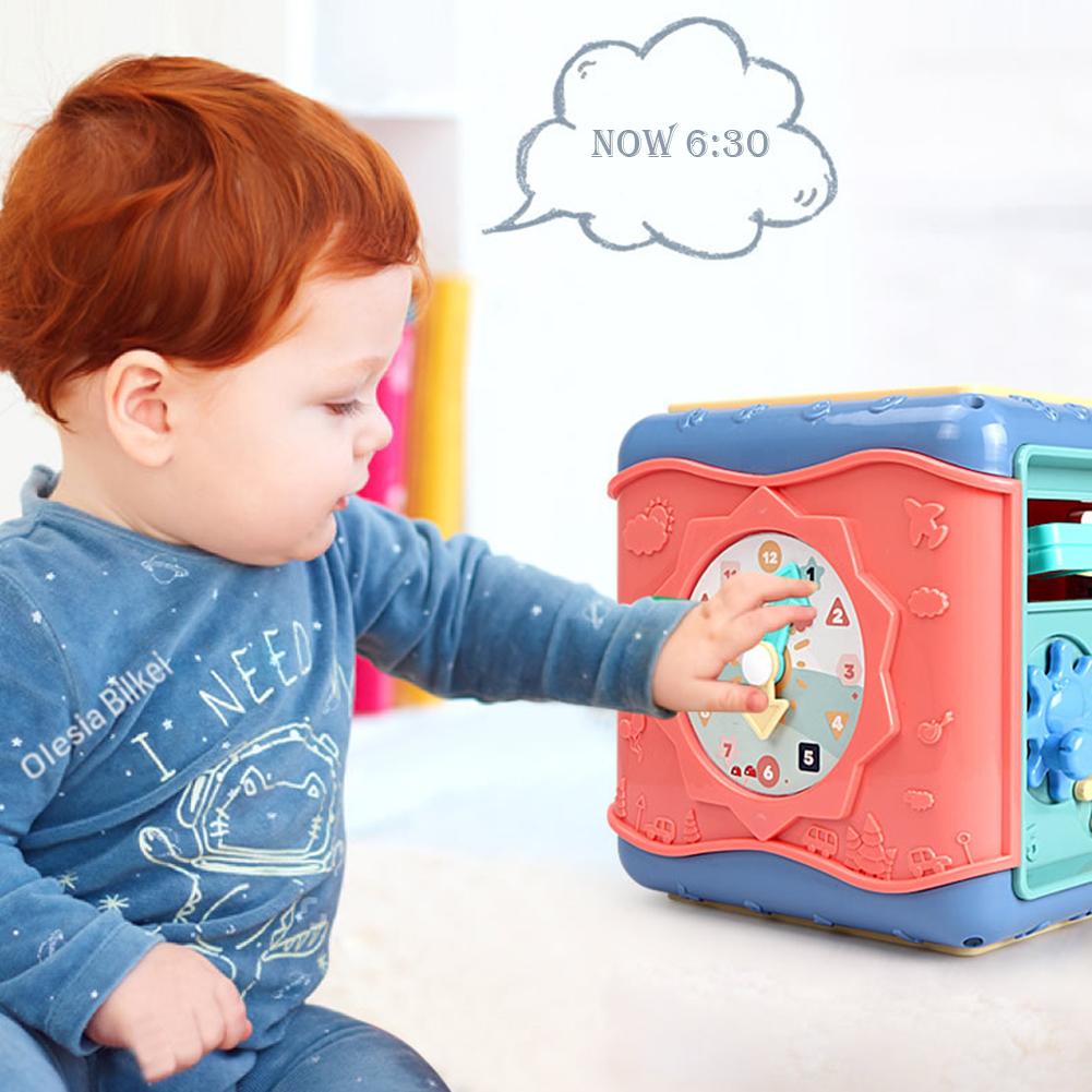 Red-haired baby playing with a blue and peach Montessori activity cube featuring a clock and gears.
