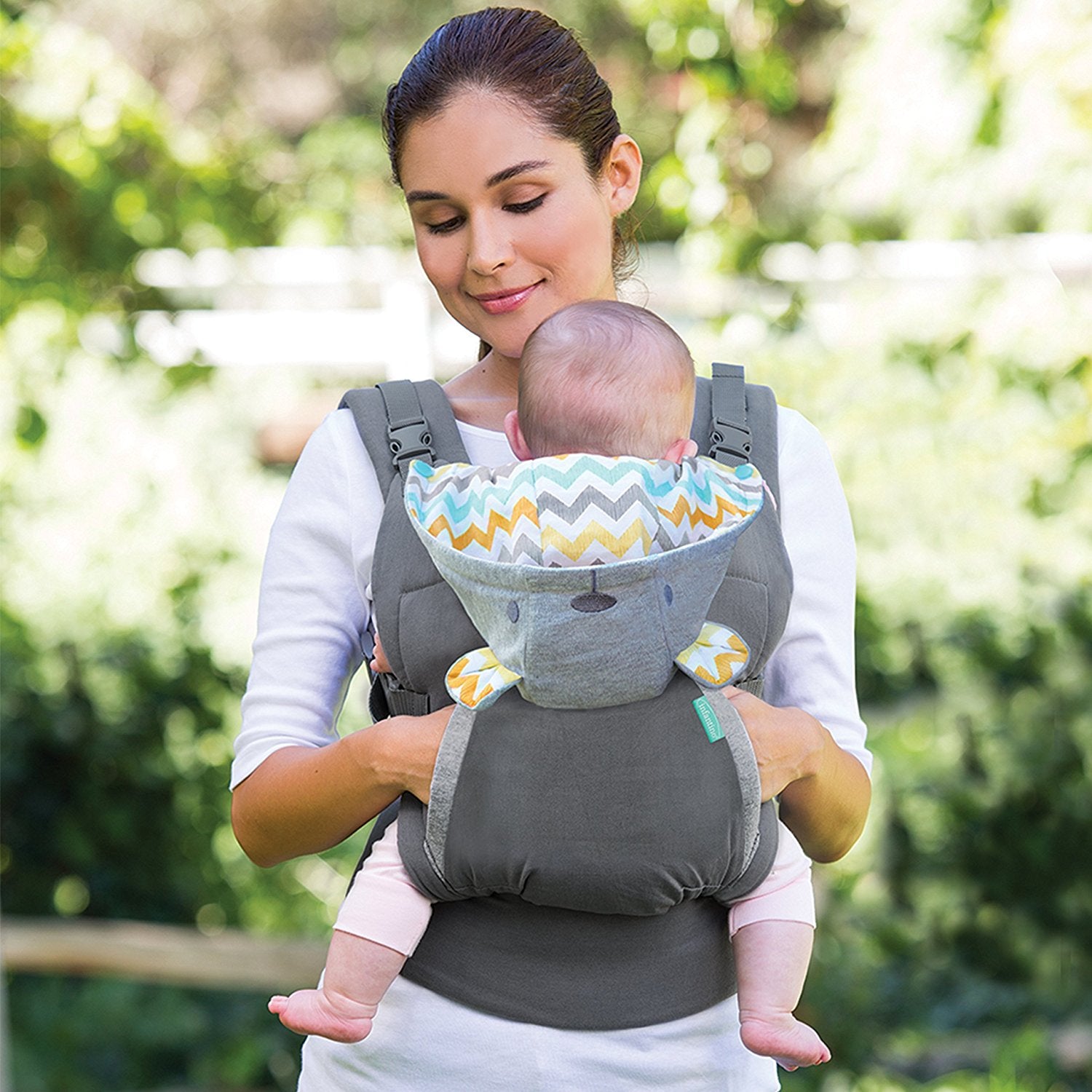 Woman carrying baby in a gray ergonomic carrier with a colorful chevron hood.