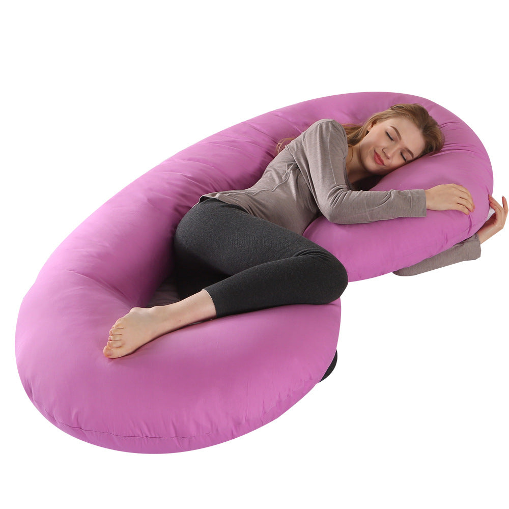 Woman sleeping soundly on a large, purple C-shaped velvet pregnancy pillow, offering full body support.