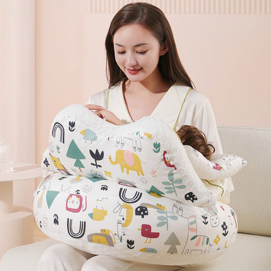 Woman holding a baby on a white, multi-functional nursing pillow with colorful animal and nature patterns.