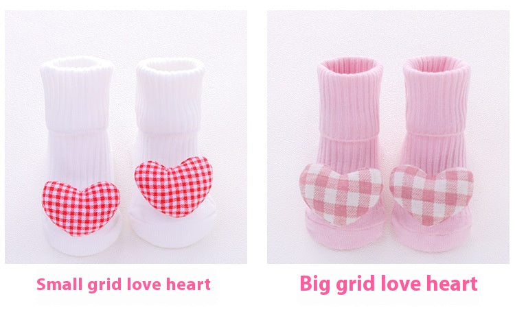 Two pairs of cotton baby socks with anti-slip soles; one white pair with small red plaid hearts, and one pink pair with large pink plaid hearts.