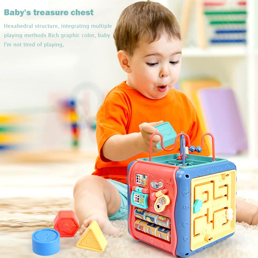 Toddler playing with a colorful hexagonal Montessori activity cube featuring a bead maze, clock, and shape sorters.