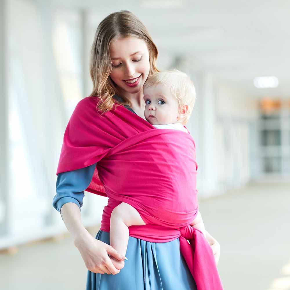Smiling mother wearing a fuchsia pink soft cotton baby wrap carrier with a blonde baby.