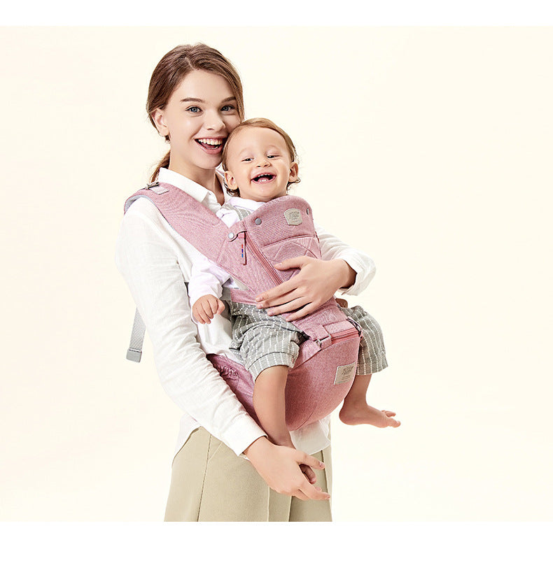 Smiling mom carrying happy baby in a pink ergonomic hip seat baby carrier.
