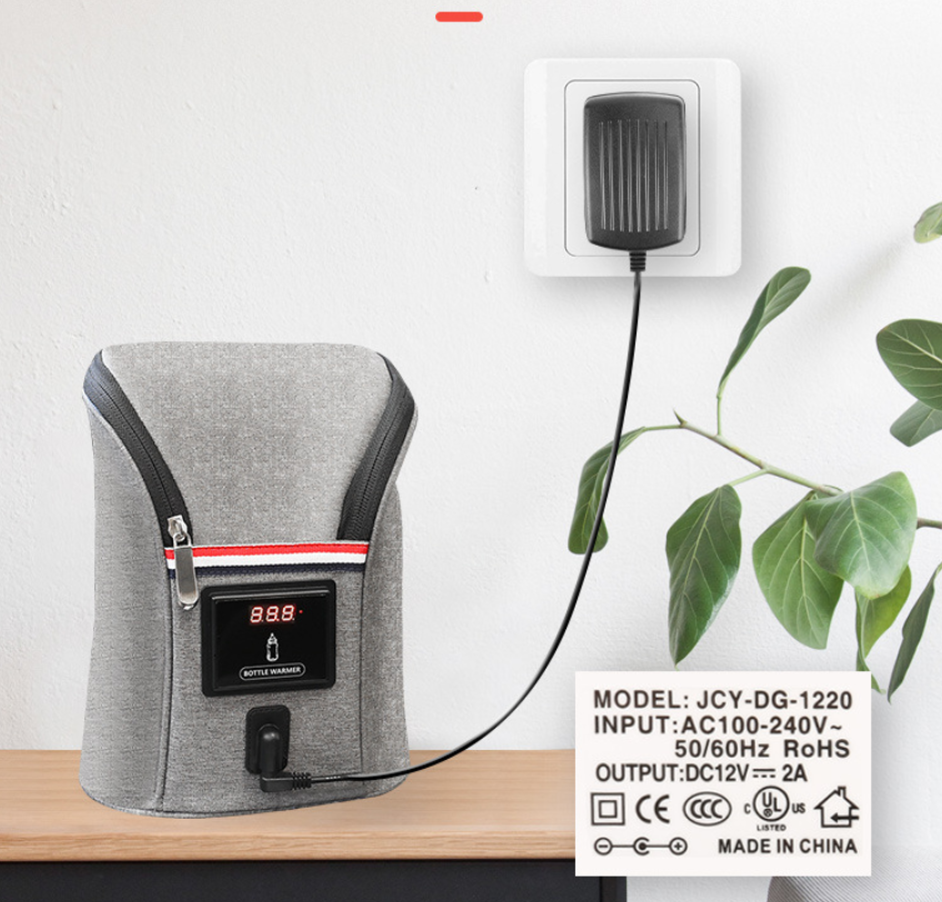 Gray portable USB car bottle warmer with digital temperature display, plugged into a wall outlet.