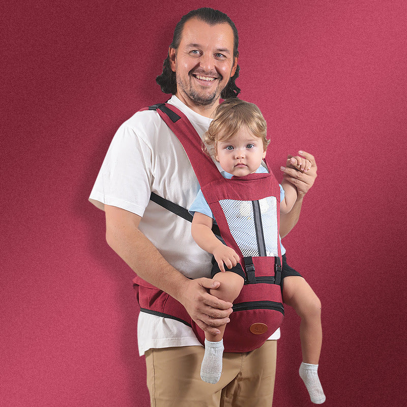 Smiling man carrying a baby in a maroon ergonomic hip seat carrier with breathable mesh.