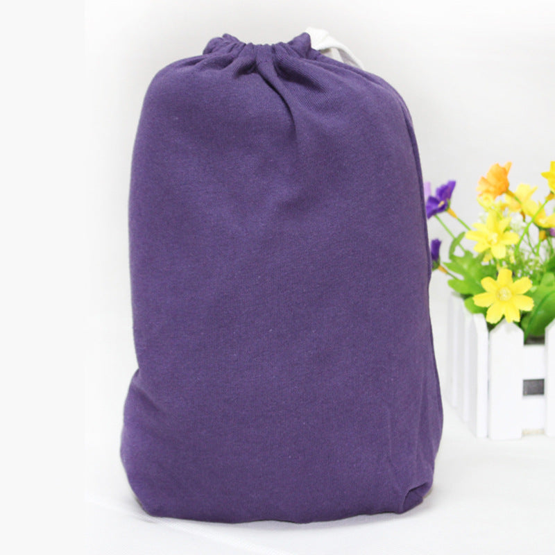 Purple cotton X-type ergonomic baby carrier folded in a drawstring bag, with flowers in background.