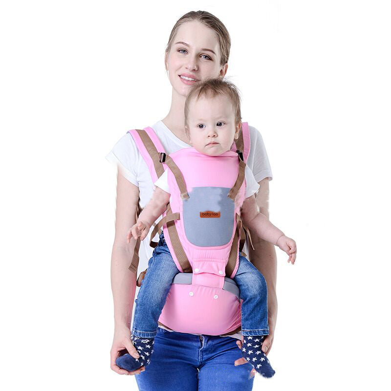 Woman carrying baby in a pink ergonomic baby carrier with a waist seat and brown straps.