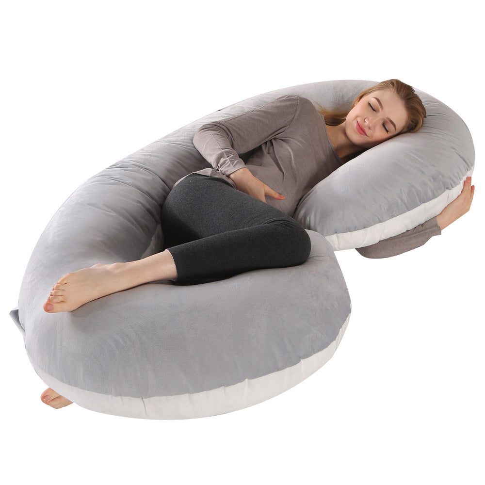Pregnant woman sleeping peacefully on a large, soft gray velvet C-shaped maternity pillow.