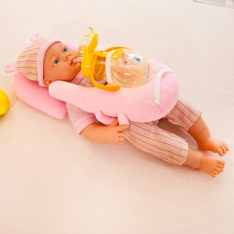 Pink velvet automatic baby feeding pillow with bottle holder, supporting a doll.